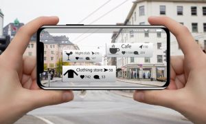La imagen, sostenida en horizontal con un teléfono inteligente, muestra etiquetas de realidad aumentada que señalan negocios cercanos, mientras apunta a una calle de la ciudad con tiendas de poca altura y peatones. Aparece un pequeño texto en pantalla, pero no es legible.