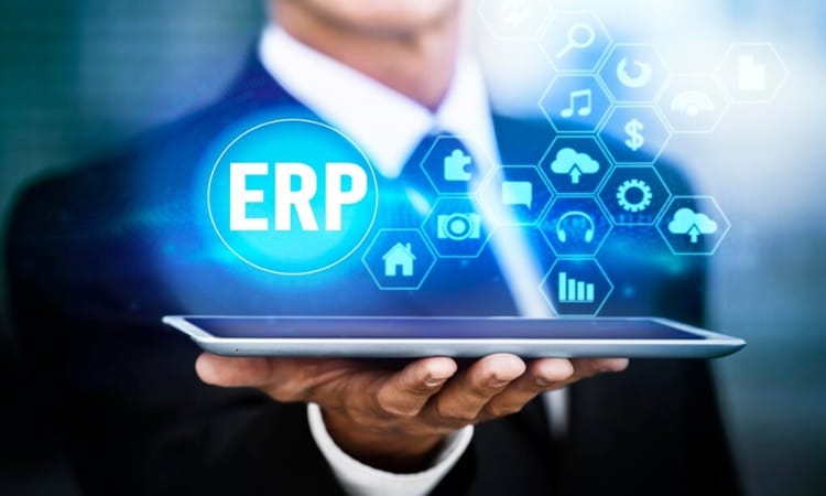 Un empresario sostiene una tableta que proyecta iconos holográficos de "ERP" y de red (nube, análisis, carrito de la compra, página de inicio) sobre un fondo de oficina borroso.