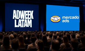 Dos grandes pantallas de proyección muestran logotipos ("ADWEEK LATAM" y "mercado ads") mientras un público sentado las observa en una sala de conferencias con poca luz, al estilo de un teatro.